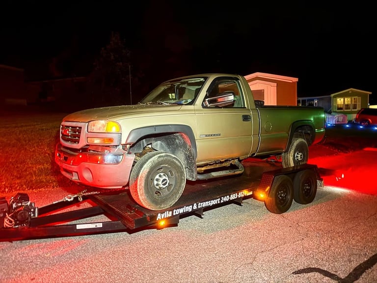 GMC truck loaded on red flatbed trailer at night with emergency lights on