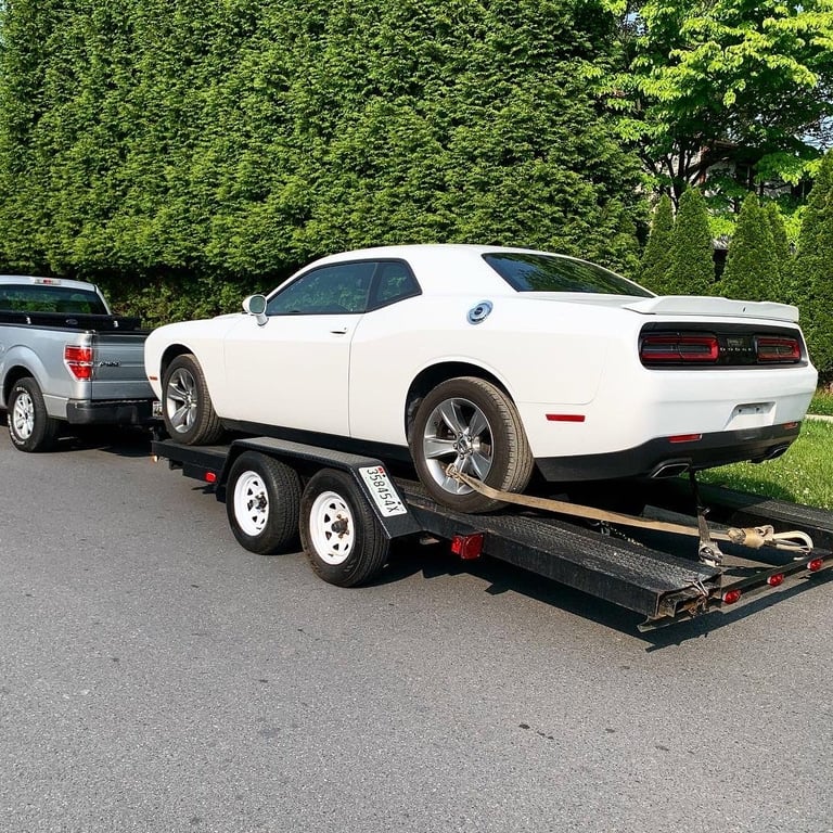 White Dodge Challenger muscle car loaded on a black enclosed car hauler trailer parked on a residential street with green hedges