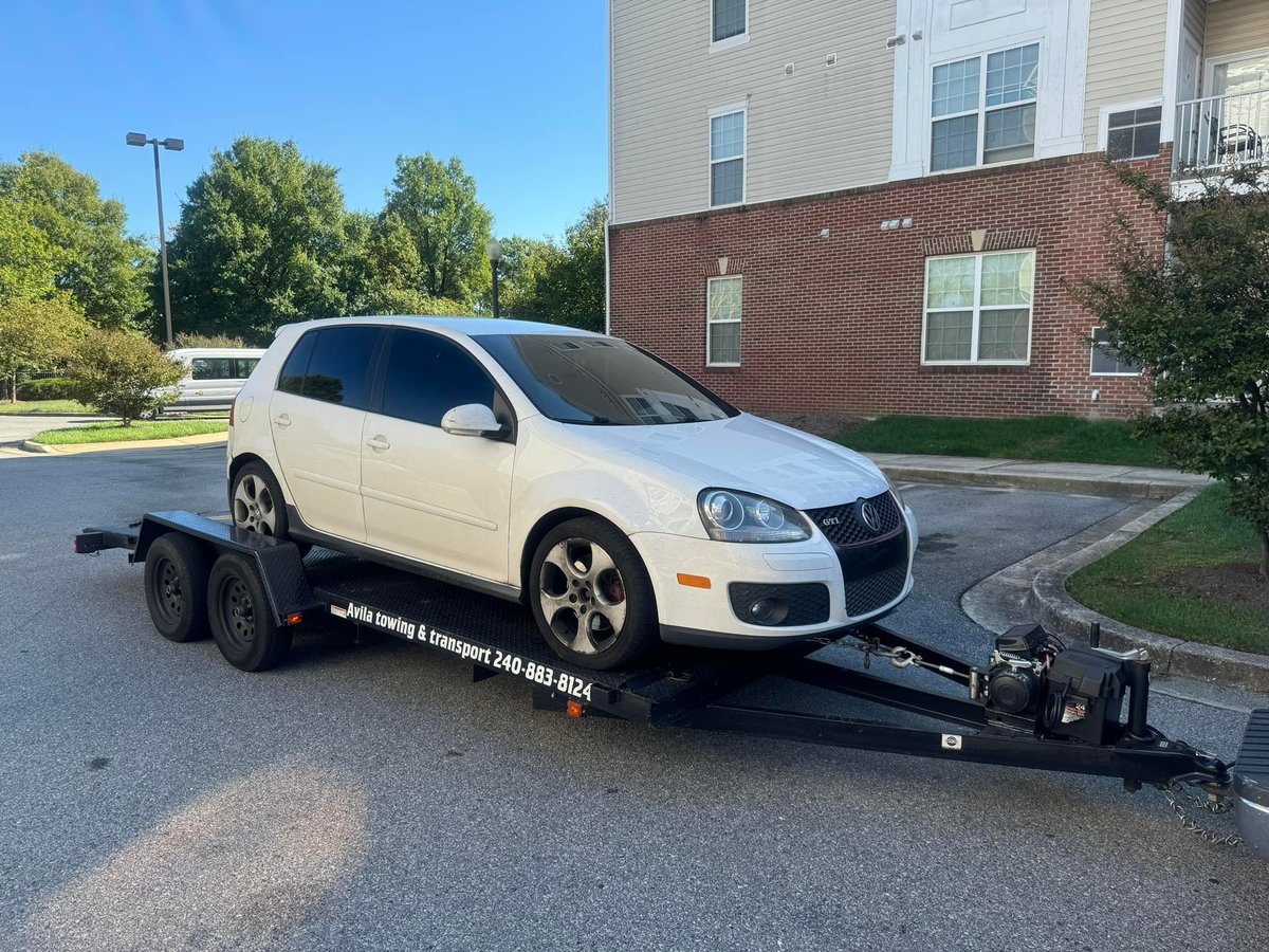 White Volkswagen vehicle loaded on a black car trailer in a residential parking lot