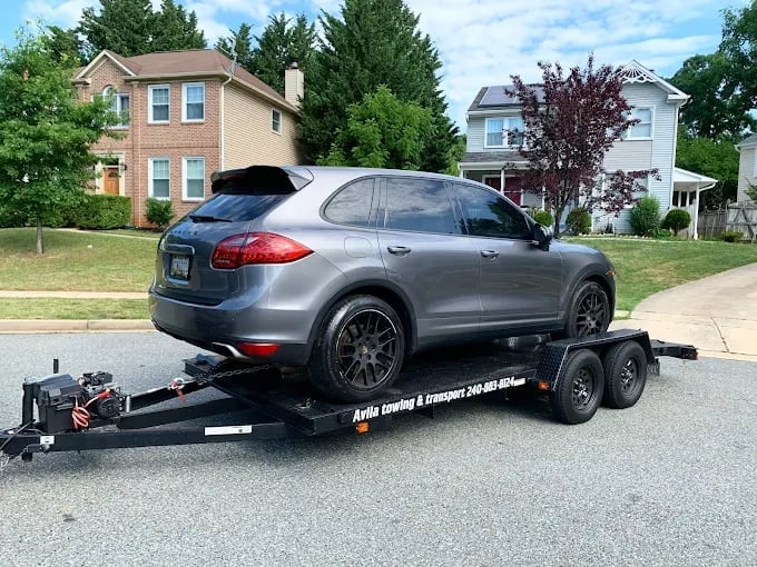 Gray SUV loaded on a black two-axle car trailer in a residential driveway