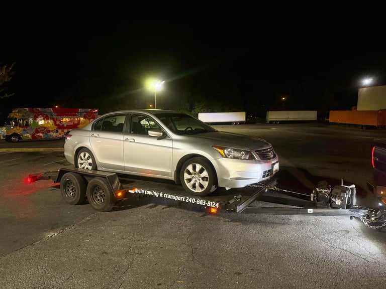Silver sedan being towed on a flatbed trailer at night in a parking lot