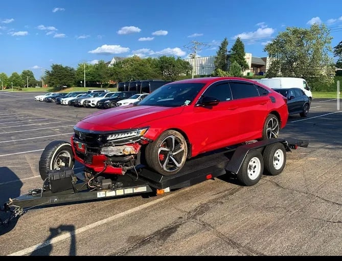 Red damaged sedan being towed on a flatbed trailer in a parking lot