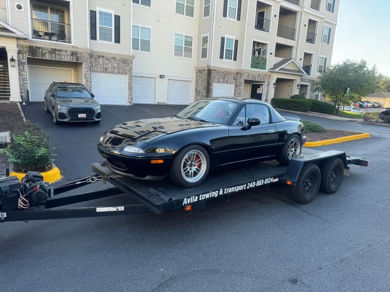 Black sports car loaded on a flatbed tow truck in a residential apartment complex driveway